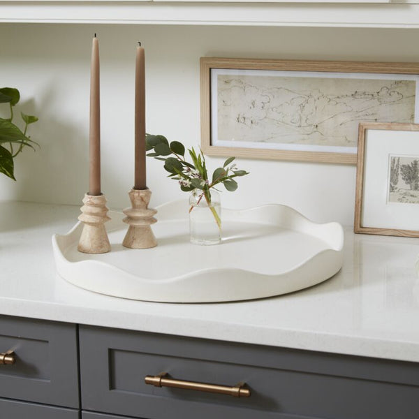 A white ceramic Elgin Tray with a unique squiggle rim, displayed on a kitchen counter with a white surface and decorative items around it.