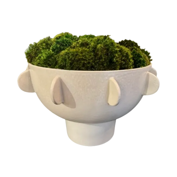 A white ceramic planter shaped like a stylized face with raised side details, filled with bright green artificial moss, shown on a plain white background.