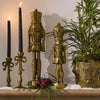 Decorative setup with gold nutcrackers, candles, and greenery on a wooden surface.
