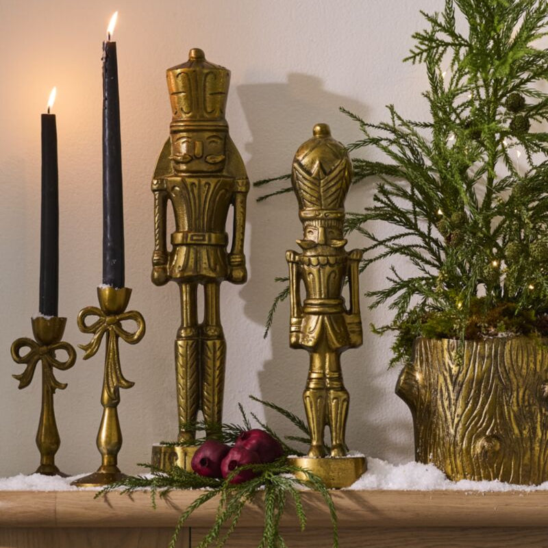 Decorative setup with gold nutcrackers, candles, and greenery on a wooden surface.