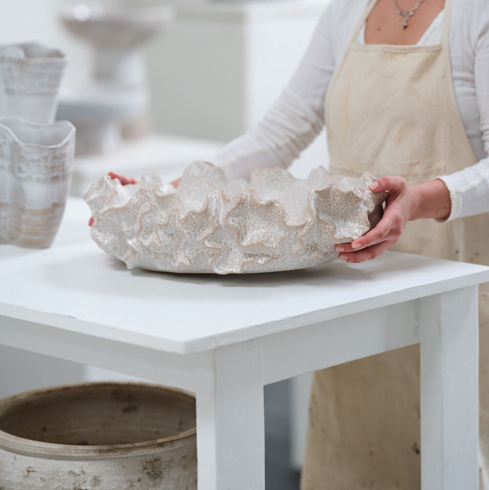 Person wearing an apron holding a textured ceramic bowl on a white table.