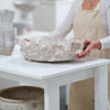 Person wearing an apron holding a textured ceramic bowl on a white table.